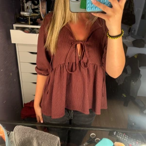  blus med knyt och volang - Supersöt ”vinröd” blus med knytband framtill och lätt volang under bysten. Blusen har trekvartsärmar med resår. Perfekt för dig som gillar en avslappnad men ändå trendig look.