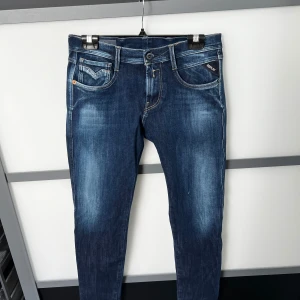 Replay Anbass blå jeans slim fit - Snygga blå Replay Anbass jeans med slim fit och klassisk femficksdesign. Jeansen har ljusa slitningar framtill och bak, samt detaljerade bakfickor med broderi. Tillverkade i stretchig bomullsdenim för en bekväm passform. 