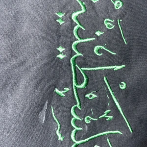 Svart hoodie med grön brodyr - Svart hoodie med grön broderad arabisk text på bröstet. Klassisk huva och känguruficka framtill. Mjuk och skön, perfekt för en chill och avslappnad stil. Brodyren ger en unik och personlig touch till din outfit.Den tö XL i barn storlek. Det står ”Palestina” på arabiska och tröjan är väldigt skön med bra kvalité.