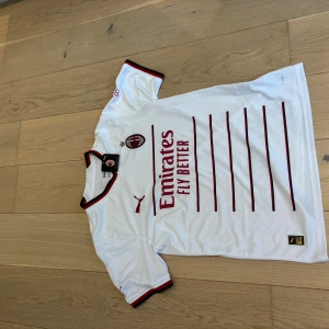 AC Milan vit bortatröja Puma - AC Milan bortatröja i vitt med röda och svarta detaljer. Puma-logga och klubbmärke på bröstet, Emirates Fly Better-tryck på framsidan och wefox på ryggen. Tunn, sportig polyester med korta ärmar och randiga muddar. Storlek M helt ny med lapp.