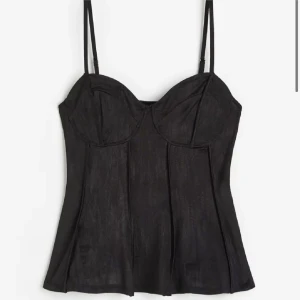 Svart korsett-topp med tunna band - Snygg svart korsett-topp med tunna axelband och markerade kupor. Toppen har en figurnära passform och sömdetaljer framtill som ger en cool och trendig look. Perfekt att styla med jeans eller kjol för en edgy vibe.