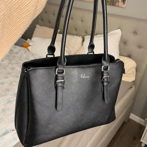Snygg Svart axelväska från Rizzo  - Stor rymlig axelväska från Rizzo. Väskan är jätte bra för att den får plats med mycket och inuti finns många fack! Älskar den här väskan supermycket men får inte användning av den längre så säljer vidare :)