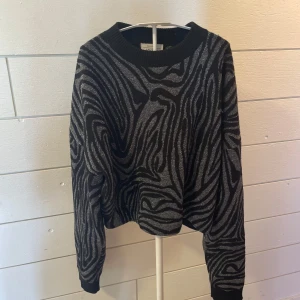 Zebramönstrad tröja & Other Stories - Snygg svart tröja från & Other Stories med glittrigt zebramönster i silver. Modellen är lite loose fit med rund hals och långa ärmar. Materialet är mjukt och stretchigt med metallictråd.