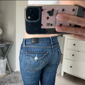 True Religion blå skinny jeans - Säljer ett par blå skinny jeans från True Religion med ikoniska bakfickor och silverfärgade knappar. Jeansen har kontrastsömmar, låg midja och klassisk femficksdesign. Materialet är stretchigt denim som sitter snyggt och bekvämt. 
