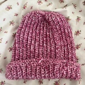 Rosa ribbstickad mössa - Säljer en chunky ribbstickad mössa i rosa och vitt melerat garn. Mössan har uppvikt kant och är riktigt mjuk och varm, perfekt för kyliga dagar. Den stickade strukturen ger en snygg och trendig look. Tråden är en fästning - inte garn som gått upp. 