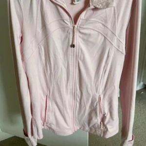 Ljusrosa lululemon define jacket - Supersnygg helt ny lululemon define jacket i färgen strawberry milkshake med figurnära passform och dragkedja framtill. Jackan har långa ärmar och två praktiska fickor med dragkedja. Perfekt för dig som gillar en clean och sportig look. Materialet känns lätt och smidigt, helt perfekt.