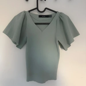 Ljusgrön topp med puffärmar Vero Moda - Superfin ljusgrön topp från Vero Moda med v-ringning och stora puffiga kortärmar. Toppen är ribbad och har en figurnära passform som ger en snygg siluett. Perfekt för dig som vill sticka ut med coola detaljer och trendig look.