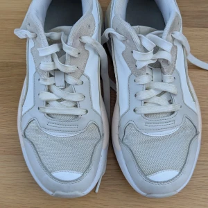 Vita sneakers från Puma strl 39 - Snygga vita sneakers från Puma i storlek 39. Skorna har en chunky sula, meshdetaljer framtill och partier i mocka och syntet. Klassisk snörning och diskret Puma-logga baktill. Perfekta för en clean och sportig look.