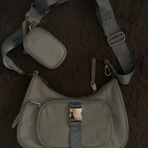 Babyblå axelväska från Steve Madden - Snygg babyblå axelväska från Steve Madden med bred axelrem och extra liten väska fäst på remmen. Väskan har ett stort fack, en framficka med spänne och dragkedja samt detaljer i silver. Perfekt för dig som vill ha en trendig och praktisk väska. Skriv för fler bilder. PRIS KAN DISKUTERAS!!🥰