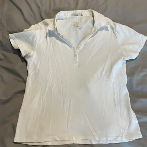 Vit kortärmad polotopp från Cecil - Vit polotopp från Cecil i storlek M. Toppen har klassisk krage, korta ärmar och knappar framtill. Tillverkad i mjuk bomull som känns skön mot huden. Enkel och stilren design som passar perfekt till jeans eller kjol.