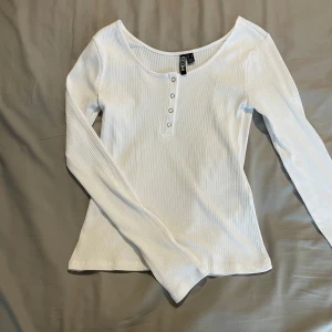 Vit ribbad långärmad tröja Pieces - Snygg vit långärmad tröja från Pieces med ribbad struktur och knappar framtill. Tröjan har en rund halsringning och är tillverkad i mjuk bomull, perfekt för en clean och stilren look.