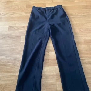 Svarta kostymbyxor med raka ben - Klassiska svarta kostymbyxor med raka ben och pressveck. Byxorna har hällor för bälte och stängs framtill. Perfekta för en stilren och clean look. Från Gina tricot