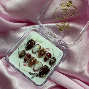 VelvetCurse (S);Short Almond - Snygga gelé press-on naglar i kort mandelform med brun, vinröd och nude bas. Dekorerade med guldfärgade pärlor och stjärnor samt vita detaljer. Kommer i storlek S: 15 mm, 11,5 mm, 12 mm, 11 mm, 9 mm. Perfekt för dig som vill ha unika och trendiga naglar.