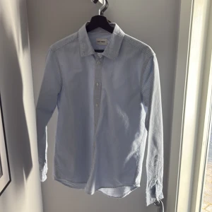 Ljusblå randig skjorta från East West - Snygg ljusblå randig skjorta från East West i storlek M.