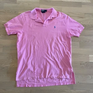 Rosa pikétröja från Polo Ralph Lauren - Säljer en klassisk rosa pikétröja från Polo Ralph Lauren i storlek L. Tröjan är i 100% bomull, har korta ärmar, krage och den ikoniska broderade loggan på bröstet. Perfekt för en chill och stilren look.