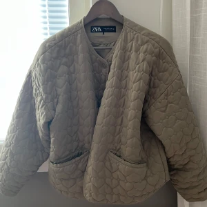Quiltad beige jacka från Zara M - Quiltad beige jacka från Zara i storlek M. Jackan har hjärtformat mönster, rund halsringning och knäppning framtill. Två fickor framtill och en loose passform ger en chill vibe. Perfekt för lager-på-lager under höst och vår.