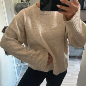 Beige stickad tröja från Gina Tricot - Supermysig beige stickad tröja från Gina Tricot med breda ribbade muddar vid ärmslut och nederkant. Tröjan har en relaxed fit och rund halsringning.