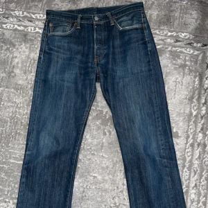 Levi's 501 blå jeans W32 L34 - Klassiska Levi's 501 jeans i mörkblå denim med raka ben och normal passform. Byxorna har fem fickor, knappgylf och snygga kontrastsömmar. Perfekta för dig som gillar tidlös stil och vill ha ett par ikoniska jeans i garderoben. Väldigt fint skick då de knappt är använda. Pris kan diskuteras. 
