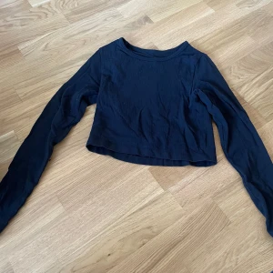 Svart ribbad croppad långärmad tröja tränings tröja  - En svart, croppad långärmad tröja med ribbad struktur. Tröjan har en enkel rund halsringning och är tillverkad i ett mjukt, stretchigt material som sitter snyggt på kroppen.  Passar även XS