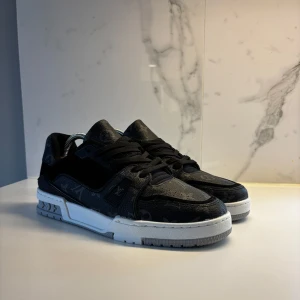 Louis Vuitton Trainers - Snygga svarta sneakers med vit sula och diskret mönster. Skorna har snörning och en rund tå, vilket ger en klassisk look. Perfekta för en stilren vardagsstil.