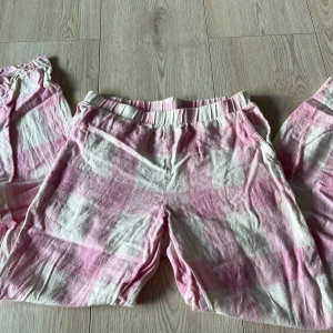 Rosa och vita rutiga byxor från Kappahl - Säljer ett par mysiga rosa och vita rutiga byxor från Kappahl. Byxorna har en elastisk midja för extra komfort och är perfekta för en avslappnad stil. De är tillverkade i ett mjukt material som känns skönt mot huden.
