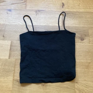 Svart linne från Gina Tricot - Säljer en enkel och stilren svart linnetopp från Gina Tricot. Toppen har smala axelband och är perfekt för sommaren eller som ett basplagg i garderoben. Köpt från Gina tricot, Storlek XS