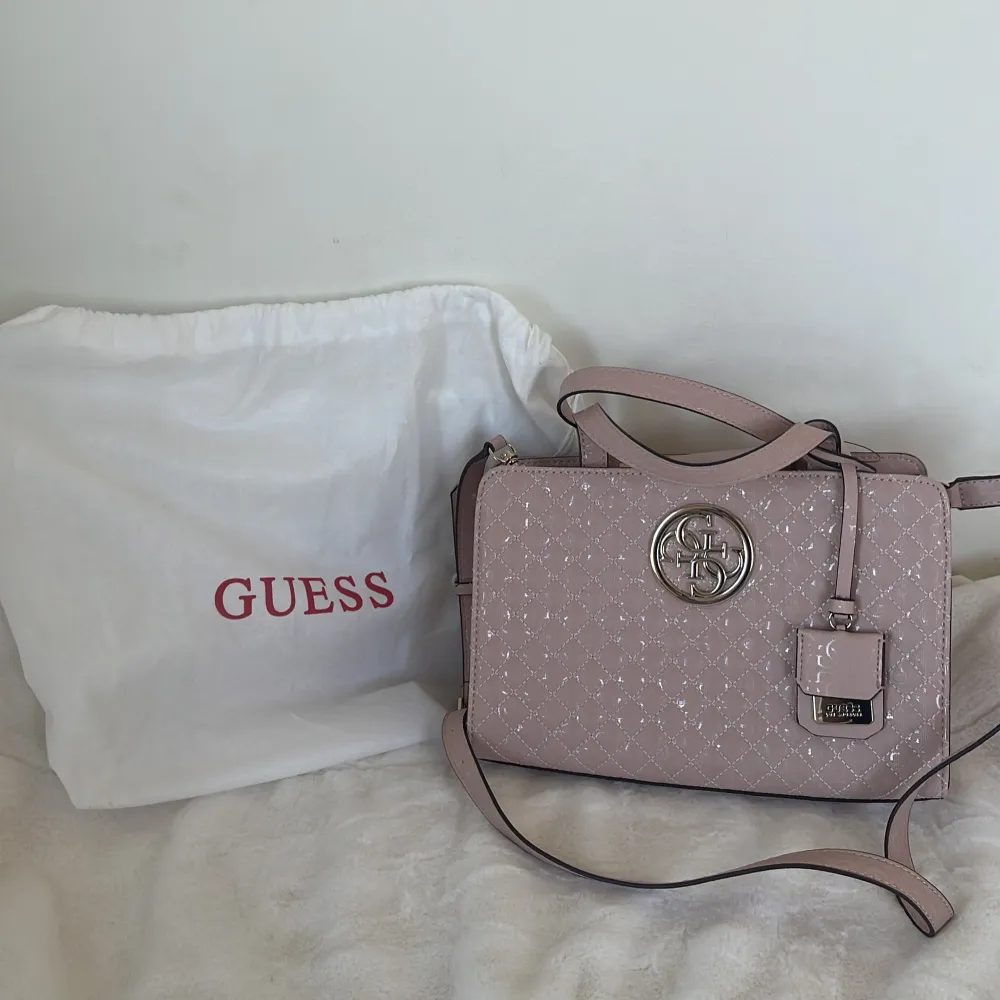 Snygg oanvänd handväska från Guess med quiltad design och ett stort metallmärke framtill. Väskan har både handtag och en avtagbar axelrem för flexibilitet. Perfekt för att bära dina dagliga nödvändigheter med stil. Har inte kvitto endast dustbag. Laukut & Käsilaukut.