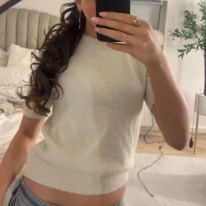 Vit stickad kortärmad tröja - Säljer en stilren vit stickad tröja med korta ärmar. Perfekt för en avslappnad look. Tröjan har en ribbad kant vid midjan för en snygg passform.