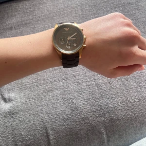 Svart och guld klocka från Emporio Armani - Jag säljer min klocka från Emporio Armani med svart urtavla och guldfärgade detaljer. Armbandet är i svart och matchar den eleganta designen. Klockan kommer med originalförpackning, manual och certifikat.
