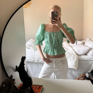 Grön rutig blus -  grön rutig blus med puffiga kortärmar och knytband vid ärmsluten. Blusen har en elastisk midja och volangdetaljer vid nederkanten.