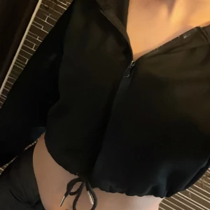 Svart croppad jacka - Snygg svart croppad jacka med dragkedja och knytning i midjan. Perfekt för en trendig look.