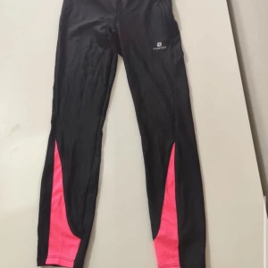 Svarta träningsleggings med rosa detaljer från Energetics - Snygga svarta träningsleggings från Energetics med iögonfallande rosa detaljer längs benen. Perfekta för gymmet eller löprundan. Tillverkade i ett stretchigt syntetmaterial för optimal rörelsefrihet.