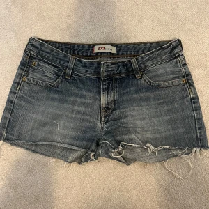 Blå jeansshorts från Levi's - Snygga blå jeansshorts från Levi's med fransiga kanter och klassisk femficksdesign. De har en låg midja. Vet inte om storleken är s eller m det står inte. 