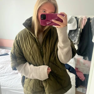 Trekvartsärmad jacka - Säljer en olivgrön quiltad jacka med korta ärmar och dragkedja framtill. Jackan har en hög krage och två fickor på sidorna. Perfekt för lager-på-lager under kyligare dagar.