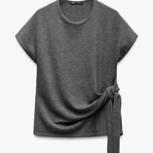 Grå topp från Zara - Snygg grå ribbad topp från Zara med korta ärmar och en unik knytning i sidan. Perfekt för en stilren look. Passar bra till både jeans och kjol.
