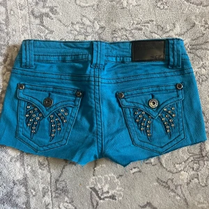 Låga Turkosa jeans shorts från Arizona - Snygga turkosa shorts från Arizona med dekorativa nitar på bakfickorna. Shortsen har en knapp och dragkedja framtill samt flera fickor. Perfekta för en somrig look!