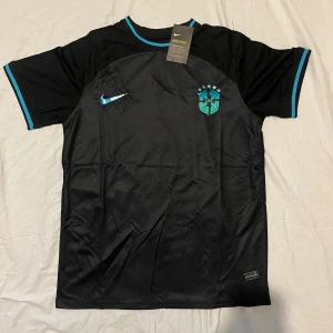 Svart fotbollströja från Nike - Snygg svart fotbollströja från Nike med blå detaljer och CBF-logga på bröstet. Tröjan är kortärmad och har en modern design med rund halsringning. Perfekt för fotbollsfans som vill ha en stilren look.