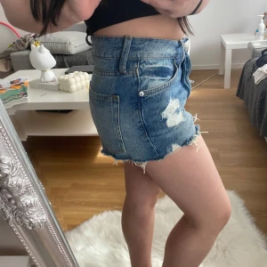 Blå jeansshorts med slitningar - Snygga blå jeansshorts med slitningar och fransiga kanter. Perfekta för en avslappnad sommarlook. De har en klassisk femficksdesign och knappgylf.