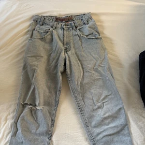 Levi's Silver Tab jeans - Säljer ett par vintage ljusblå Levi's Silver Tab jeans med en lite baggy passform. De har en sliten look med revor på ena benet och fransiga kanter. Perfekta för en casual stil.