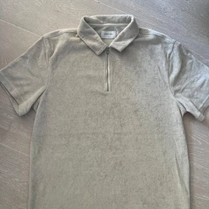 Beige frotté pikétröja med dragkedja - Ny snygg  beige pikétröja från Studio Total med korta ärmar och dragkedja framtill. Perfekt för en avslappnad stil. Tröjan har en klassisk krage och är tillverkad i ett mjukt frotté material. Rök och djurfritt hem. Aldrig använd! 