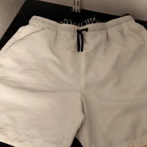 Vita badshorts från Calvin Klein - Snygga vita shorts från Calvin Klein med svart snörning i midjan. Perfekta för en avslappnad stil. Tillverkade i ett lätt och bekvämt material.