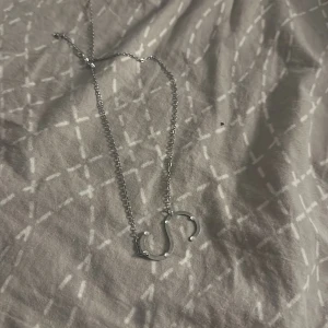 Silverfärgat halsband med bokstavshänge - Elegant silverfärgat halsband med ett hänge i form av en bokstav. Perfekt för att lägga till en personlig touch till din stil. Kedjan är tunn och smidig, vilket gör den lätt att bära varje dag.