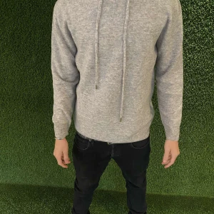 Merinoull Hoodie  - Säljer en stilren grå hoodie med dragsko i huvan. Perfekt för en avslappnad look. Tröjan har långa ärmar och ribbade muddar vid ärmslut och nederkant.