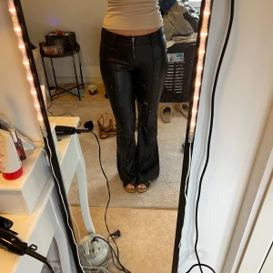  skinnbyxor bootcut lågmidjade från new yorker  - Snygga svarta skinnbyxor med låg midja och dragkedja fram. Byxorna har en tight passform och är perfekta för en trendig look. De är tillverkade i ett glansigt material som ger en cool och edgy stil. Har tecken på andvändning som på sista bileden men syns bara om man lyfter upp tyget över 