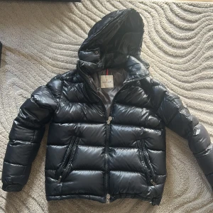 Svart pufferjacka från Moncler - Snygg svart pufferjacka från Moncler med huva och dragkedja. Jackan har långa ärmar och två framfickor med dragkedjor. Perfekt för kyliga dagar. Priser kan diskuteras 