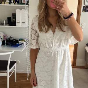 Vit spetsklänning med v-ringning - Säljer en vacker vit klänning i spets med v-ringning och trekvartsärmar. Perfekt för sommarens fester eller studentfirande. Klänningen har en fin passform med markerad midja och ett romantiskt blommönster.
