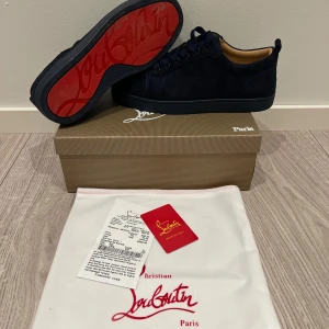 Christian Louboutin - Snygga svarta sneakers från Christian Louboutin i mocka med den ikoniska röda sulan. Skorna har snörning och en rund tå, vilket ger en stilren look. Perfekta för dig som vill ha en touch av lyx i vardagen.