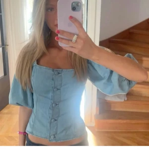 Blå jeanskorsett med puffärmar - Säljer en snygg blå jeanskorsett med puffiga ärmar och knappar framtill. Perfekt för en trendig look. Från HM och säljs inte längre. Hör av dig vid intresse! 💙