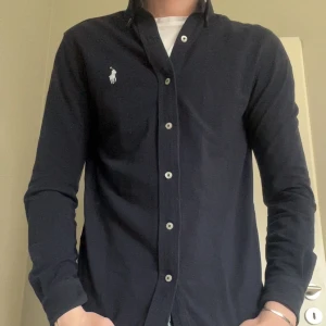 Ralph Lauren skjorta  - Snygg mörkblå skjorta från Ralph Lauren i de jätte sköna materialet mesh. Skjortan har en broderad logotyp på bröstet och är tillverkad i ett lätt och bekvämt material. Storlek Xs men passar S, Modellen är 182 cm och väger 64 kg, köpt på NK för 1700 kr, säljer för 499 kr