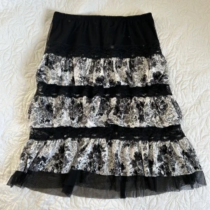 Svart och vit volangkjol - Säljer en unik svart och vit volangkjol med blommigt mönster. Kjolen har flera lager av volanger och en elastisk midja för bekväm passform. Perfekt för att ge en romantisk touch till din outfit.